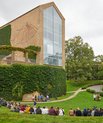 [Translate to English:] Ny studerende ses siddende i Universitetsparken i Aarhus med aulaen, der rejser sig i baggrunden.