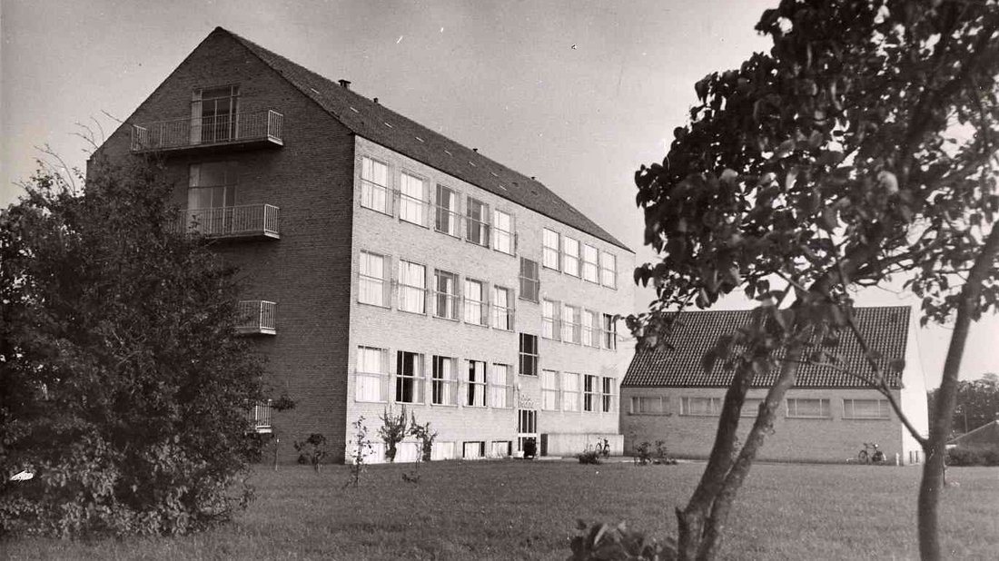 Billedet er i sort-hvid og viser bygningen fra en skå vinkel med en græsplæne i forgrunden.