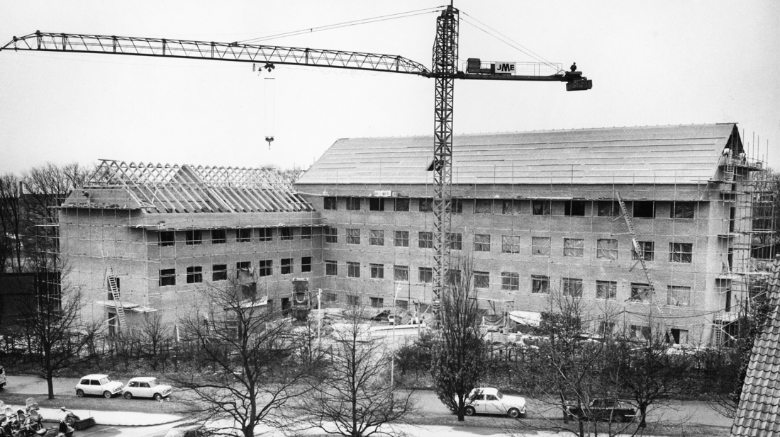 Sort/hvid foto. Bygningen ses under opførelse med en kran i forgrunden.
