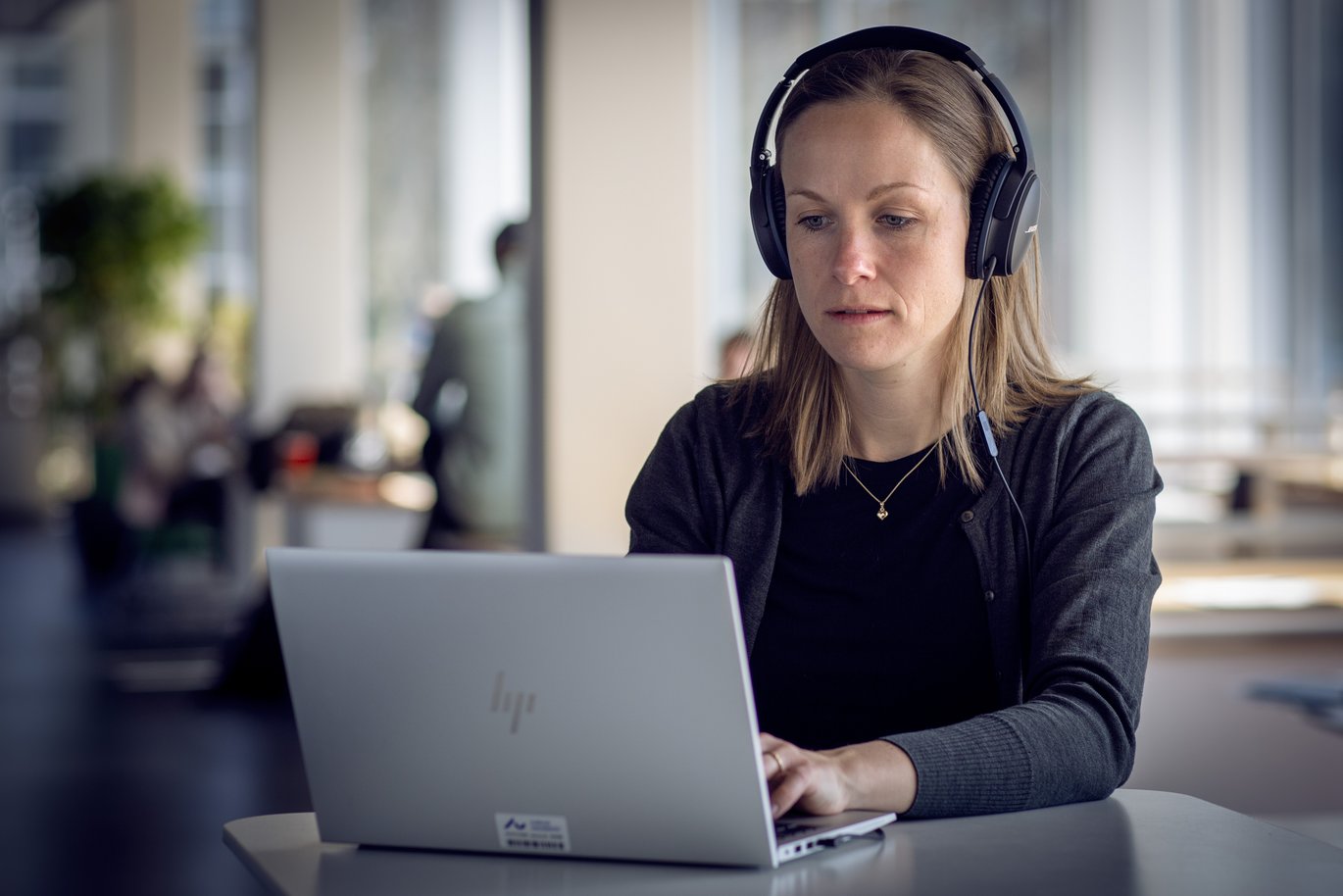 [Translate to English:] Kvinde sidder foran computer med høretelefoner og ser dybt koncentreret ud.