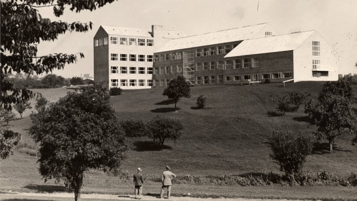 Sort/hvid foto af den første universitetsbygning med et bakket græsareal i forgrunden.