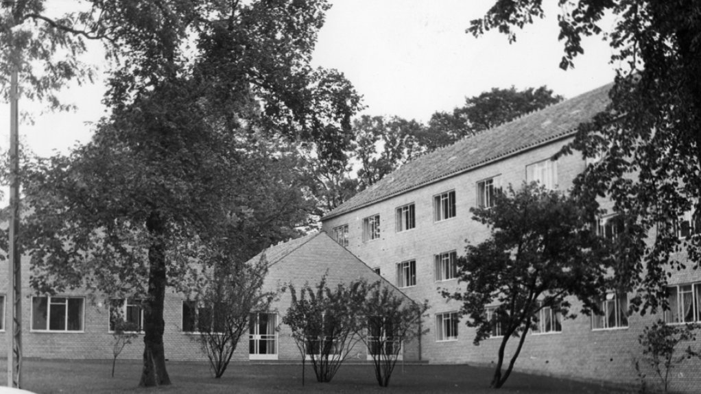 Sort/hvid foto af bygningskompleks 1650 med græsareal og træer i forgrunden.