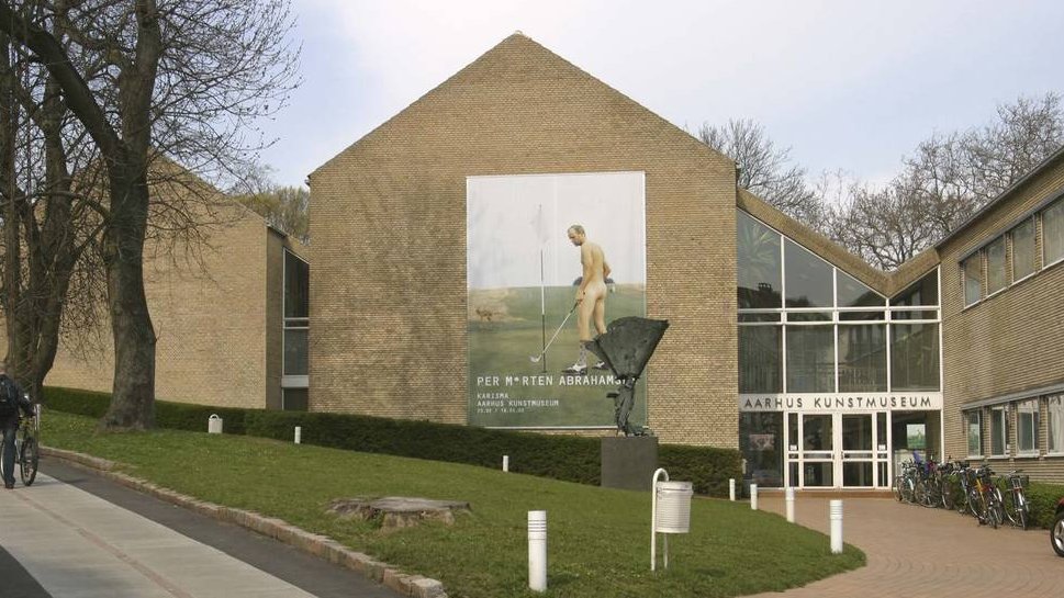 Daværende Aarhus Kunstmuseum fra indgangssiden med billede af aktuel udstilling på en gavlmur.